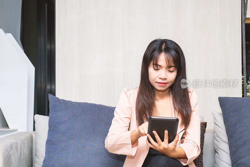 接近商务女性的手使用智能手机平板电脑打字和触摸白色屏幕的应用程序设备工作老式风格坐在大堂办公室的沙发上。