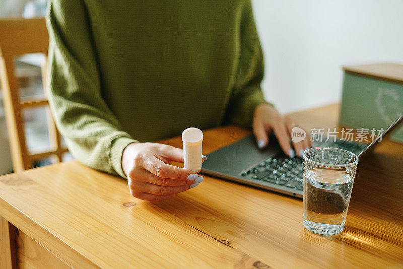 拿着药瓶使用电脑的妇女