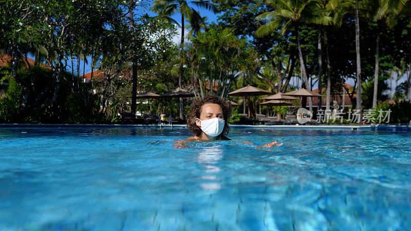 一名戴着防毒面具的女子在一座私人别墅的游泳池里游泳。她每天都安静地休息，远离喧嚣的世界。在covid-10大流行期间旅行。