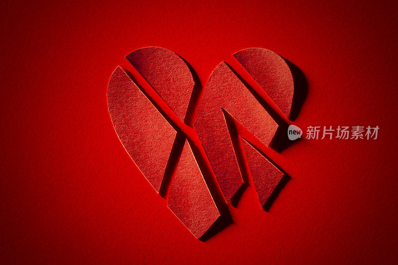 破碎的心。红色背景上的红色剪纸心形。