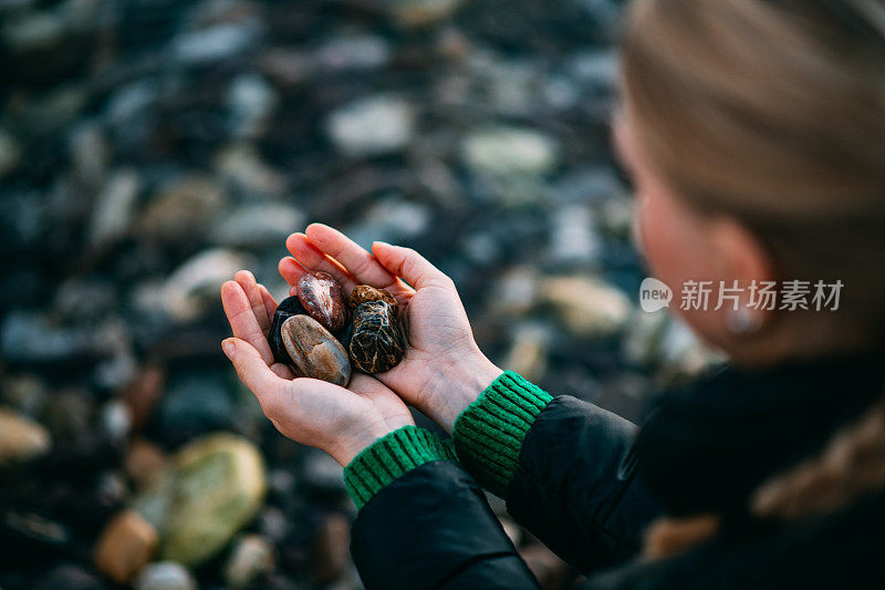 年轻女子在海滩上收集鹅卵石