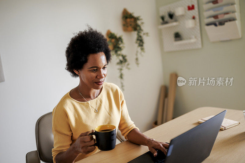 中年成年非洲妇女使用笔记本电脑和喝咖啡在家里办公室