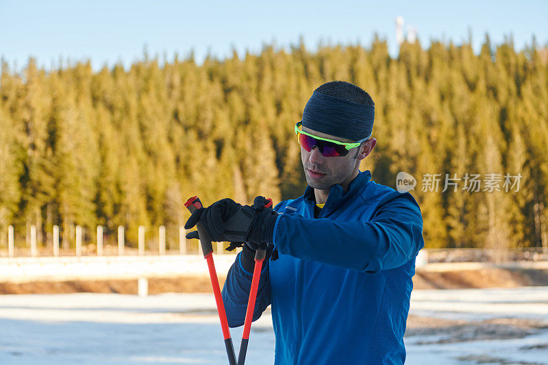 帅气的男运动员越野滑雪板，呼吸新鲜空气，在雪林艰苦训练后休息。检查smartwatch。健康的冬季生活方式