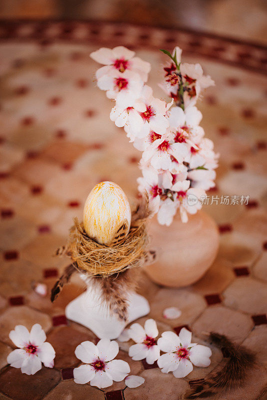金色的复活节彩蛋在一个金色的鸟巢上，在一个白色的柱子上，在一个古老的石桌子上，有杏仁花