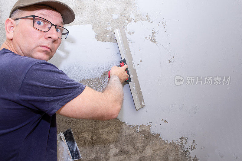 建筑工人是一个白人，他用施工抹子把腻子涂在墙上。