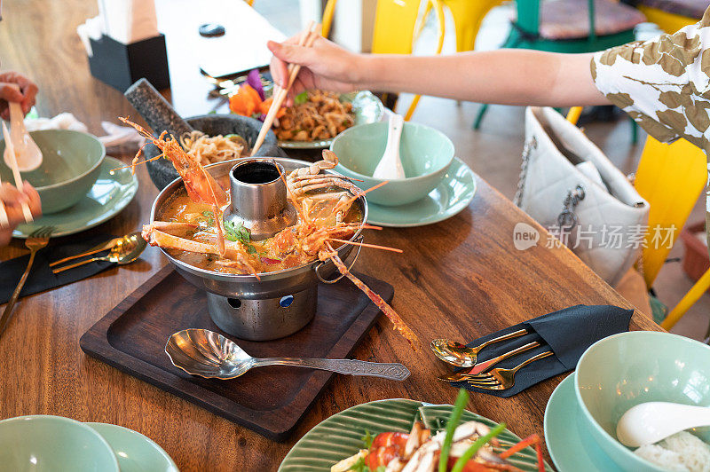 一名妇女在餐馆里吃着泰式冬阴功汤，里面有海鲜和蔬菜