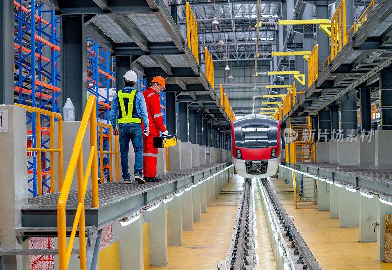 广角专业工程技术人员在工厂工作场所，走在电气或空轨列车的铁轨旁，对列车进行检查和维护。