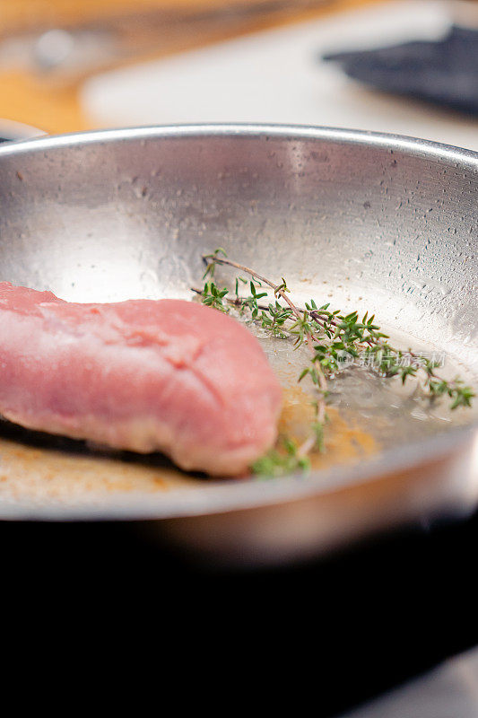 在热煎锅上加入迷迭香的粉色鸭胸肉的特写