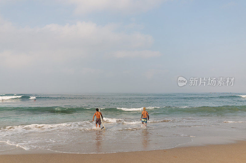 两名男性冲浪者扛着冲浪板奔向大海