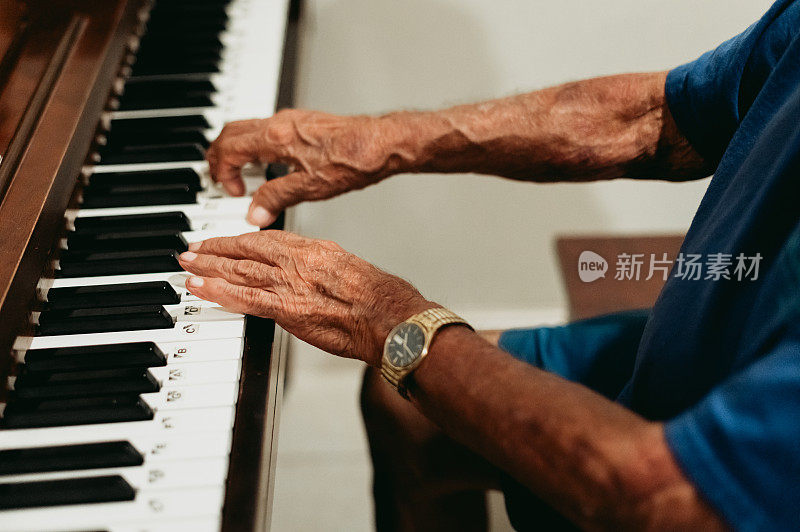 年长的成年男子双手若有所思地弹奏着一架立式钢琴