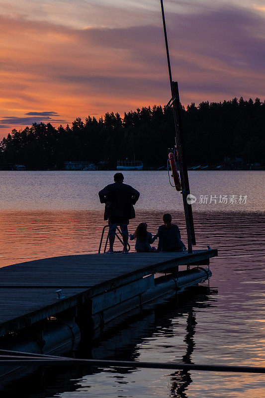 一个家庭，妇女和一个孩子在斯堪的纳维亚的一个湖上欣赏日落。地球上的夏天。