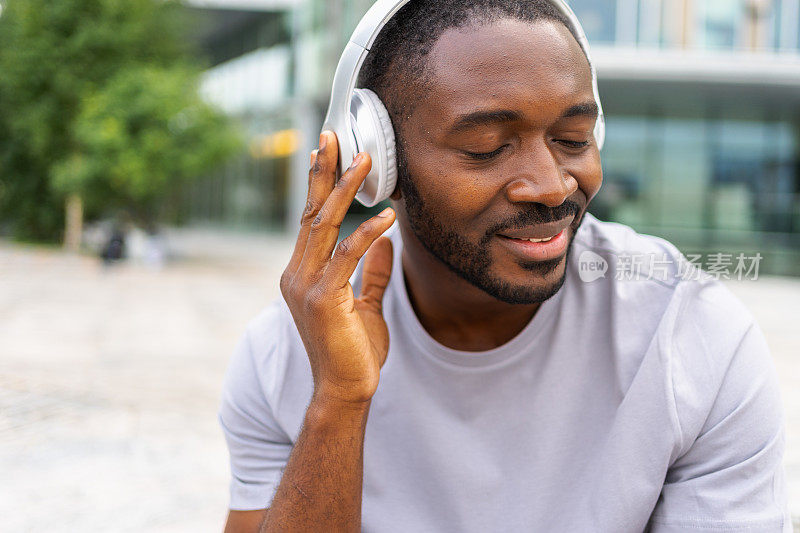 音乐歌曲概念。好的开始。快乐的非裔美国人在城市街头听着现代音乐。戴着耳机的人喜欢在户外听自己喜欢的音乐。人们的生活方式快乐。