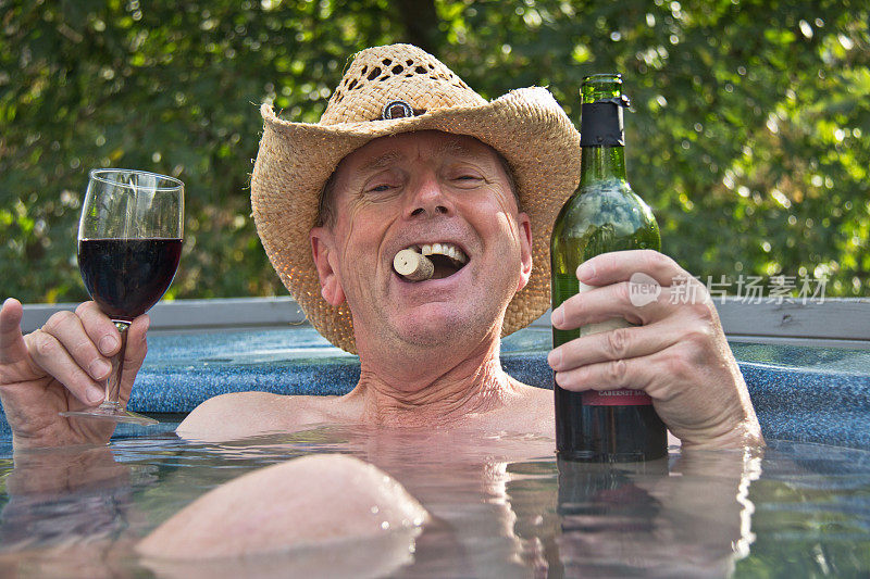 戴着牛仔帽的男人坐在热浴盆里喝着酒。