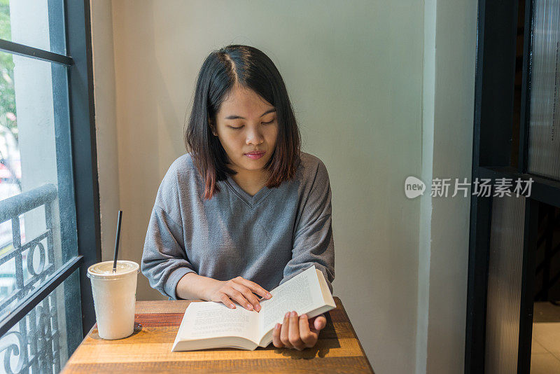 亚洲年轻女子在灰色衣服看书，喝咖啡