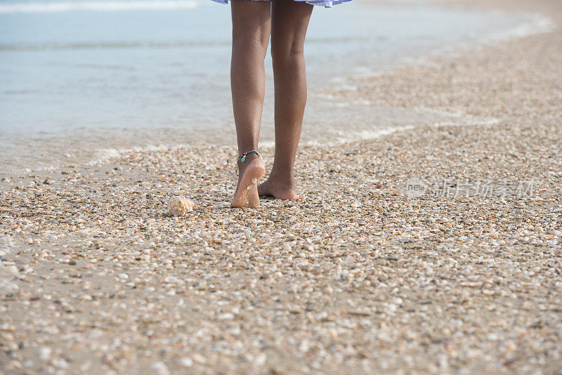 一个陌生的女人走在贝壳海滩上。