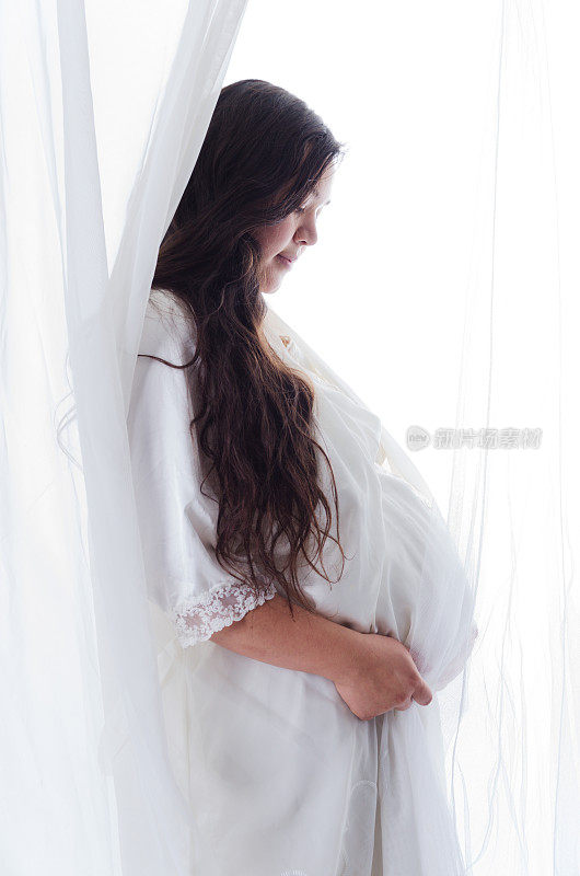 孕妇的侧面在白色的透明窗帘。