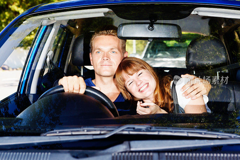 幸福的年轻夫妇坐在车里，微笑着依偎在一起