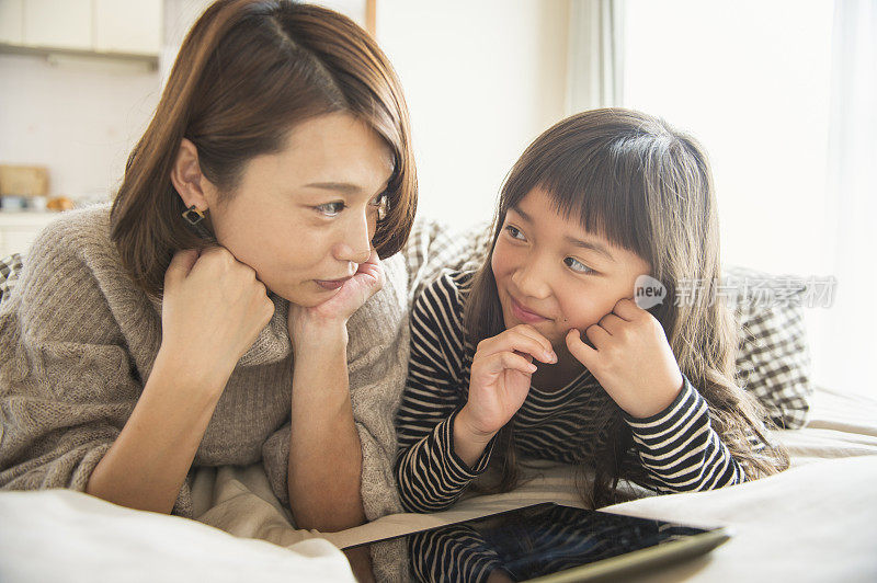 母亲和女儿在卧室玩电子平板电脑