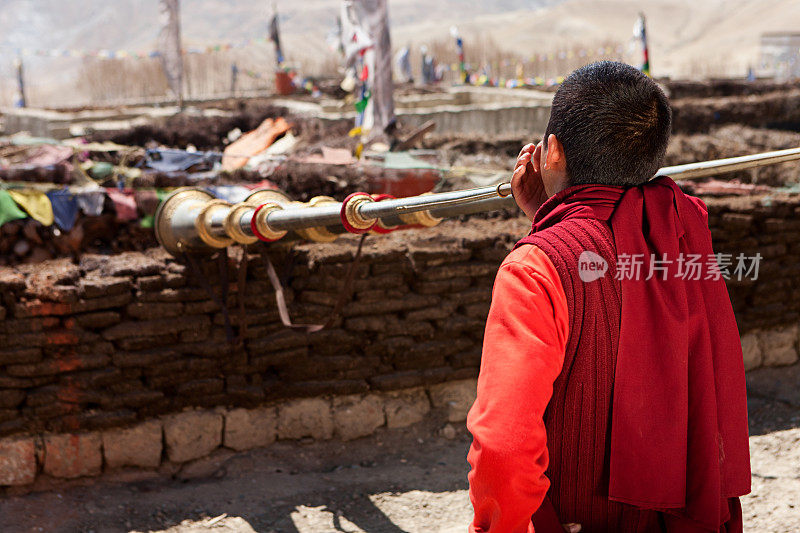 年轻的藏传僧人在屋顶上吹奏佛角，罗曼塘