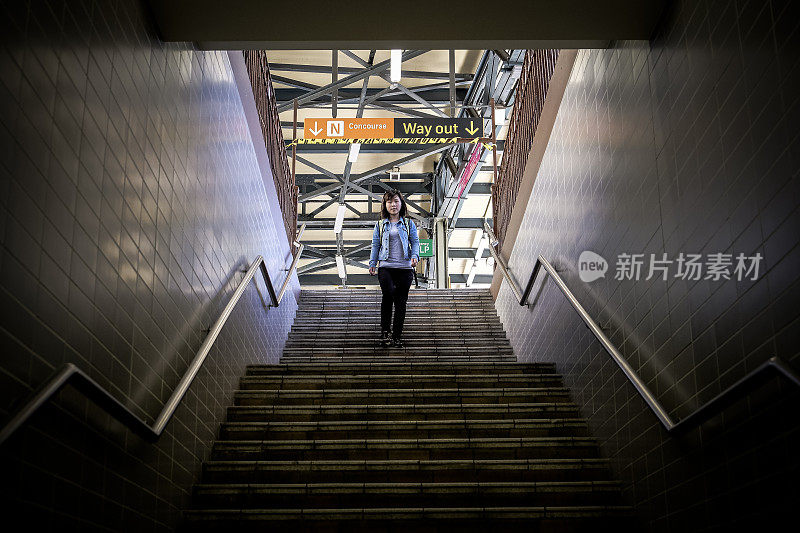 年轻的亚洲成年女子走下地铁台阶，走进黑暗