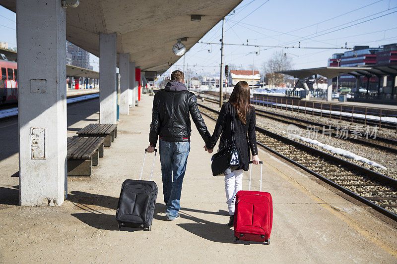 一对年轻夫妇提着行李箱等火车……火车站