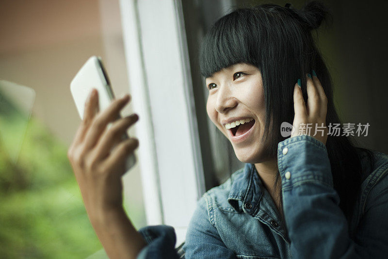 亚洲少女使用手机，而坐在靠近窗户。
