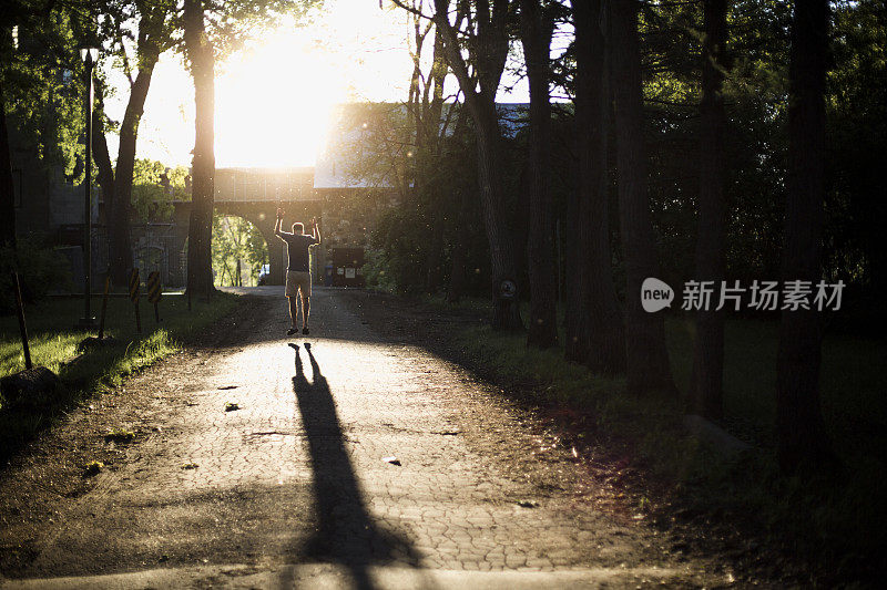 夕阳西下，一个人举起双臂在小路上跳来跳去