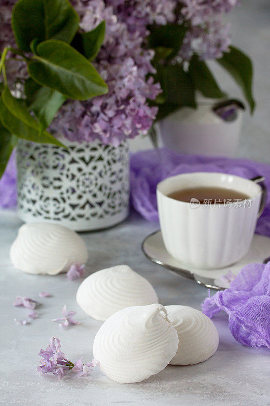 精致的香草棉花糖放在精致的白色盘子里。有棉花糖的静物画，一杯淡紫色的茶，背景是古老的石头。