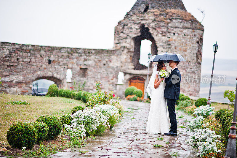 新婚夫妇在雨中带着伞漫步古塔的背景城堡