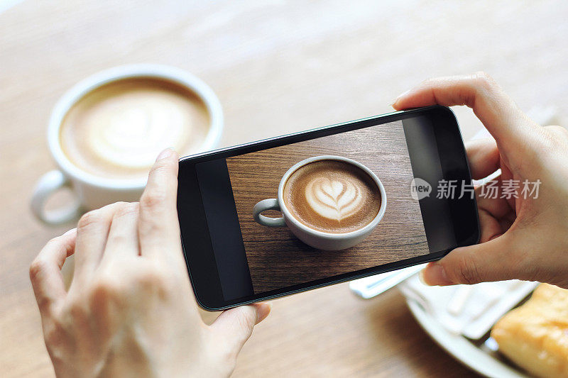 用手机拍摄木桌上的拿铁咖啡杯，咖啡生活方式。