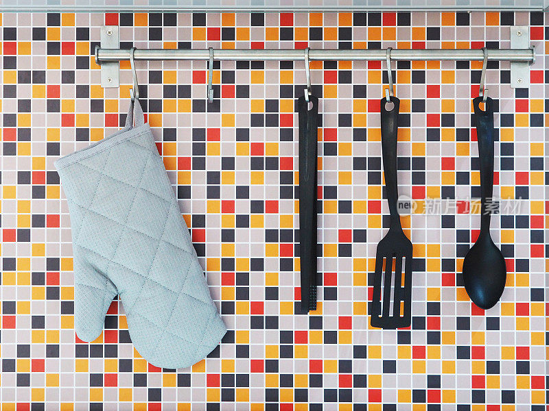 厨房用具挂在五颜六色的马赛克墙砖上。