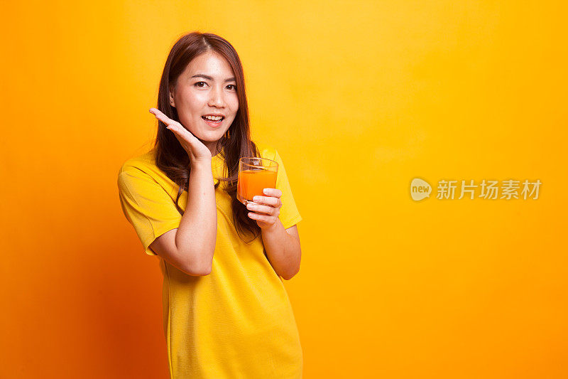 快乐年轻的亚洲女人喝橙汁在黄色的裙子