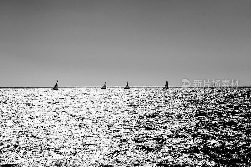 小帆船在银色的海洋中，当太阳低垂的时候。采用单色银色效果，对称构图