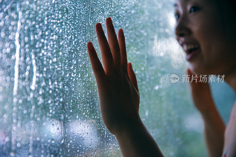 在雨天，年轻女子用手触摸窗户