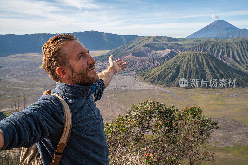 在印度尼西亚，年轻人徒步旅行，手臂伸开站在火山的山顶上，人们旅行的乐趣，冒险的概念，成功和成就