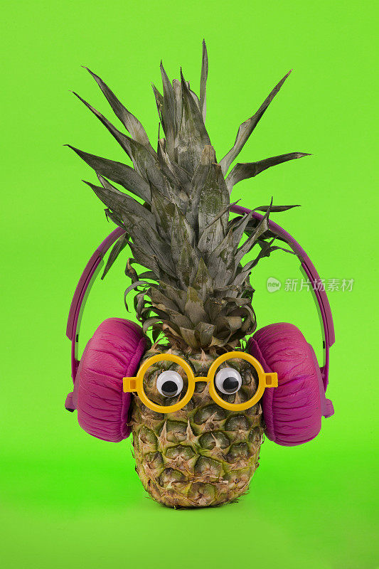 时髦的新鲜菠萝与眼镜和耳机在绿色背景。