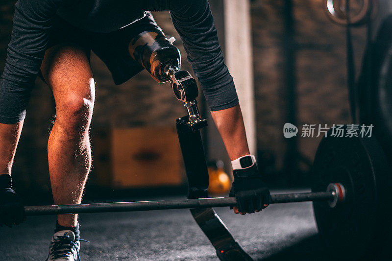 适应性男运动员用假腿做一个死气沉沉的举杠铃在健身房里