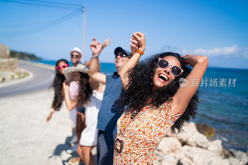 在希腊扎金索斯的海滩上，一群游客举着手臂站着