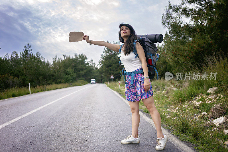 路上的旅行者女孩。手持空白纸板标牌的女性徒步旅行者。