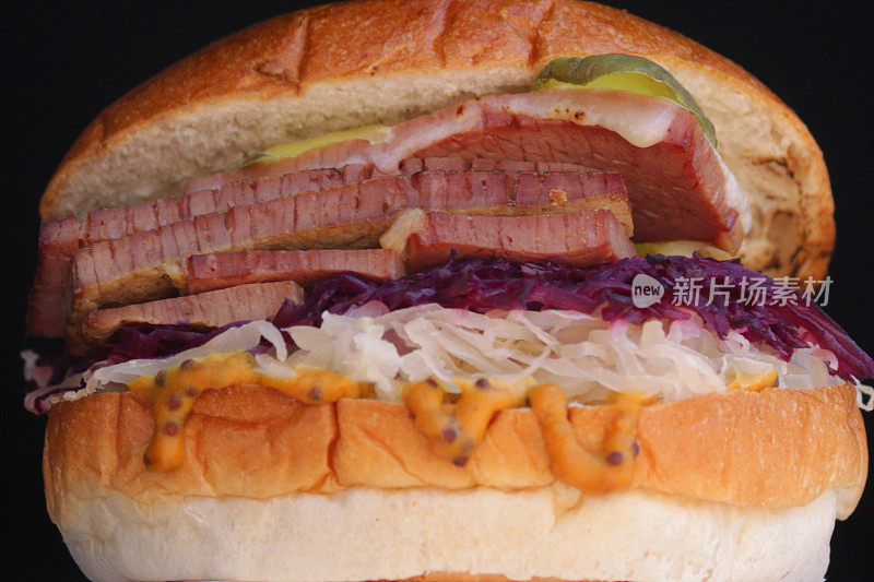 这是自制烤牛排三明治的特写，夹在面包卷里，在烧烤街的小吃摊上吃着，配上沙拉、紫菜丝、炸洋葱、芥末酱、融化的奶酪和小黄瓜片