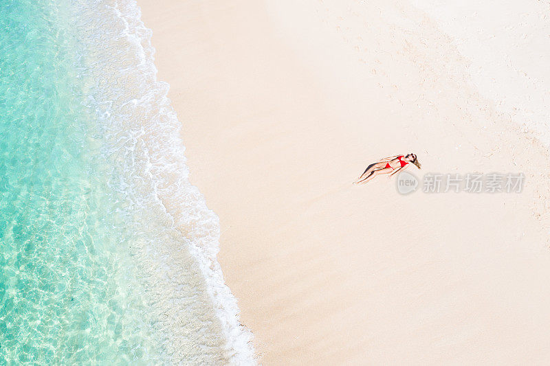 巴厘岛，年轻女子在白色沙滩上晒太阳，旁边是透明的绿松石海。空中无人机拍摄。
