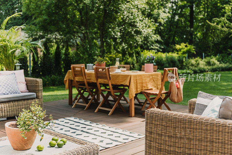 模糊的视野，橙色桌布的餐桌站在绿色花园的木制露台上