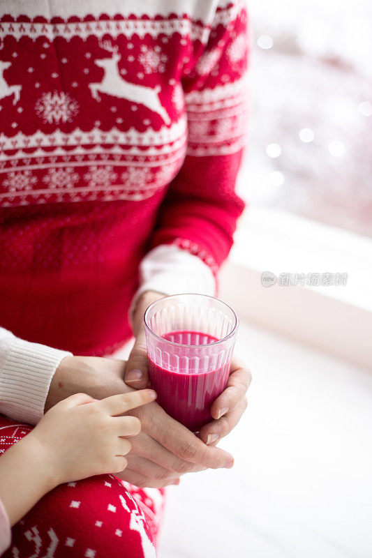 女人用手把石榴汁从瓶子里倒进玻璃杯里。附近有几颗石榴。圣诞风格背景