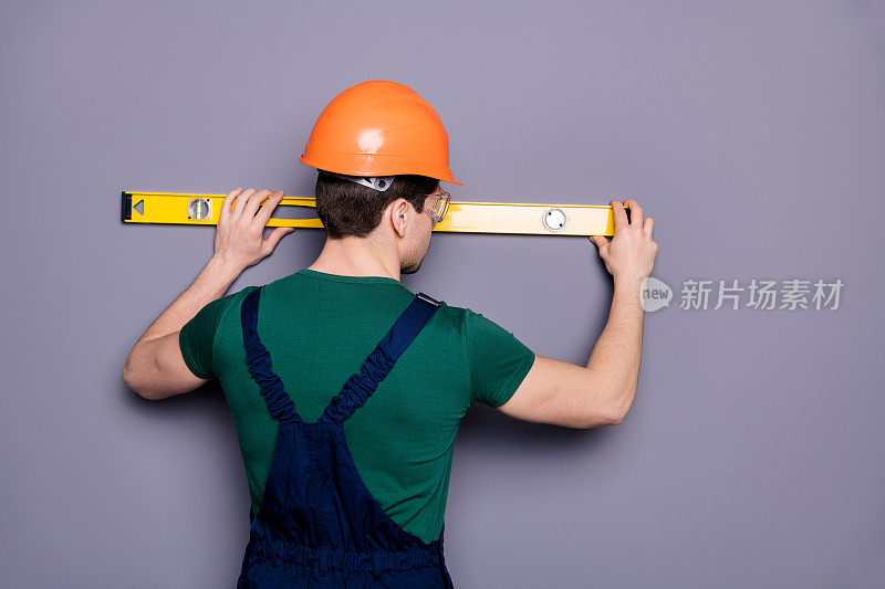 背影背影的照片英俊的男性工人男人熟练的工程师测量墙的架子长度穿t恤安全的粗布工作服防护头盔眼镜孤立的灰色背景