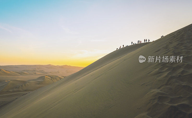 在沙漠的沙丘上攀爬山顶达到目标的一组人