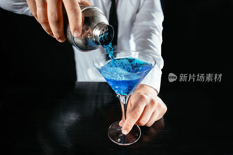 调酒师将蓝色鸡尾酒倒入马提尼酒杯