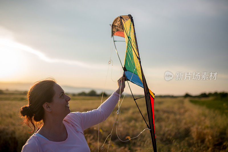 一个快乐的年轻女子，在夏季日落的林间空地上牵着风筝奔跑