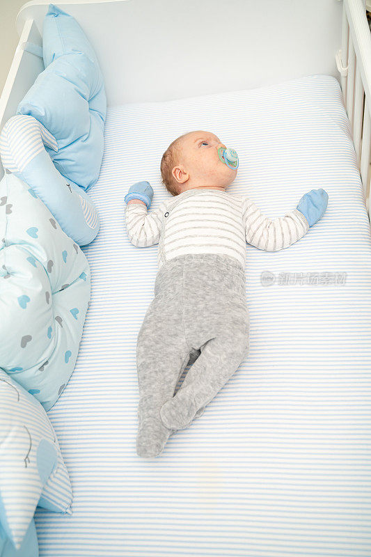 可爱的婴儿躺在他的婴儿床上吮吸着奶嘴看着摄像机的宽俯视图拍摄垂直
