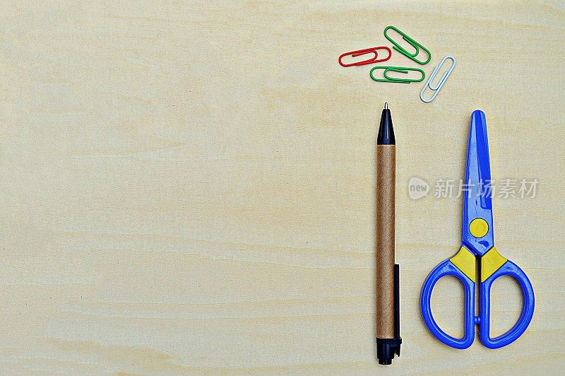 木色背景上的钢笔、彩色回形针和塑料剪刀的水平照片