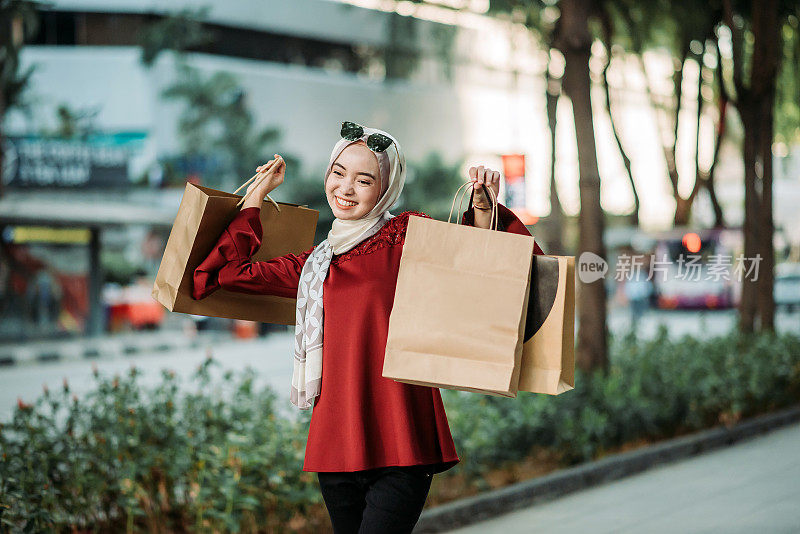 亚洲年轻的马来人女性手拿购物袋和拍照在城市街道